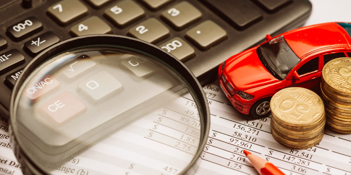 Magnifying glass over the calculator and financial report with car and coin.
