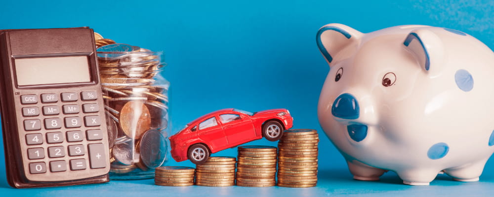 Car over the coin stack with calculator; glass jar; ceramics piggybank against blue background